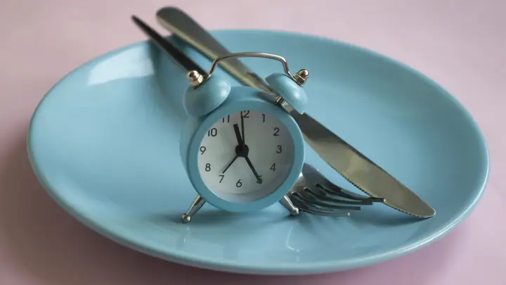 Relógio despertador sobre um prato com talheres